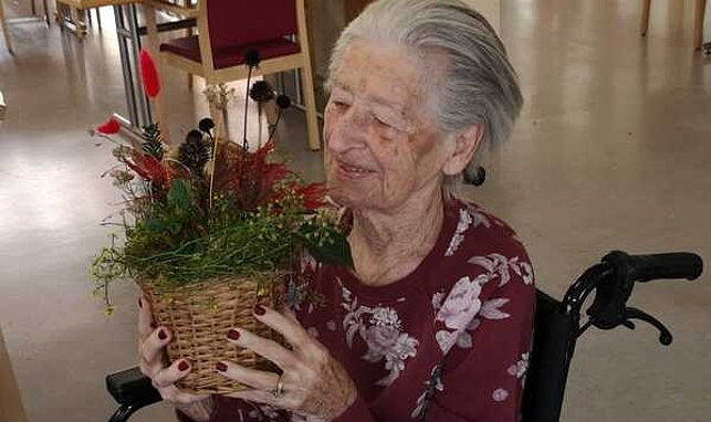 Frau im Rollstuhl hält Blumengesteck in der Hand.