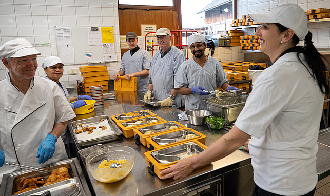Teamwork - gemeinsam werden die Warmhalteboxen für Essen auf Rädern mit regionalen Gerichten befüllt.